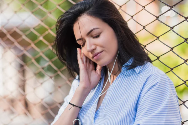 Close-up retrato de mulher morena atraente com desfrutar da música na rua da cidade. Jovem morena bonito mulher vestindo camisa azul e ouvir a música . — Fotografia de Stock