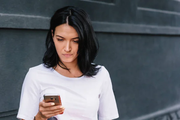 Belle femme dans des vêtements élégants, lit de bonnes nouvelles sur le téléphone mobile à l'extérieur, avec une connexion Internet haute vitesse. Messages d'adolescentes sur les réseaux sociaux. Personnes, mode de vie et concept d'entreprise . — Photo