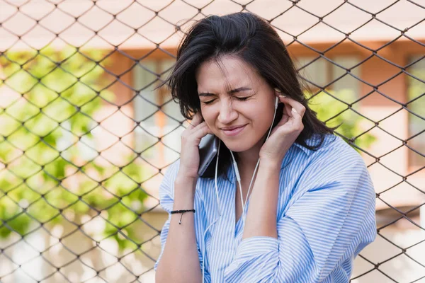 Beautiful brunette woman with earphones on the city street. Young brunette smiling business woman holding ears of loud music. People,lifestyle concept