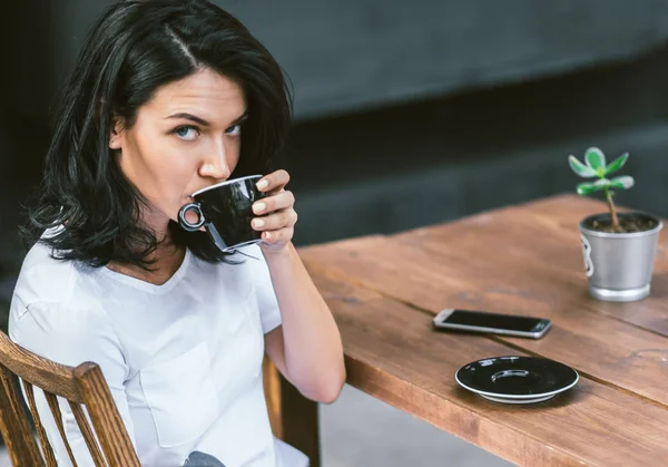 Portrait of beautiful brunette Caucasian holding mug with coffee and enjoying nice weather relaxing alone in modern coffee shop at terrace. People and lifestyle concept. — Stock Photo, Image