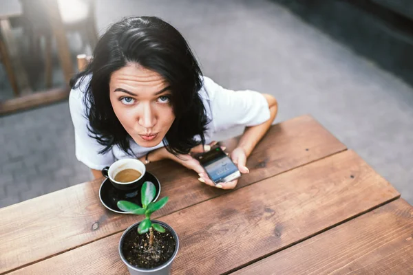 Sevimli beyaz kadın teras kafede oturan, kahve içme ve ücretsiz kablosuz internet bağlantısı akıllı telefonunu kullanarak çevrimiçi iletişim zevk hoş neşeli gülümseme ile Üstten Görünüm — Stok fotoğraf