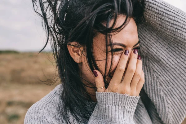 Closeup recortado retrato de mulher morena feliz e engraçada sorrindo e rindo com a mão na boca, contra fundo prado natureza com cabelo ventoso. Pessoas, viagens e conceito de estilo de vida. Humor de cobertura . — Fotografia de Stock