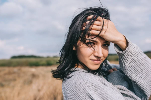 Viagens, pessoas e conceito de estilo de vida. Horizontal retrato de bela mulher sorridente vestindo suéter sendo brincalhão com vento soprando cabelo e despreocupado posando no céu luz solar e fundo do prado . — Fotografia de Stock