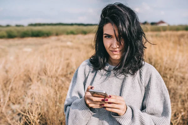 Mulher morena caucasiana usando telefone inteligente para mensagens de texto e conexão sem fio para a vida social, contra o fundo da natureza com cabelo ventoso, sorriso e sentir-se livre. Espaço para cópia. Conceito de pessoas . — Fotografia de Stock