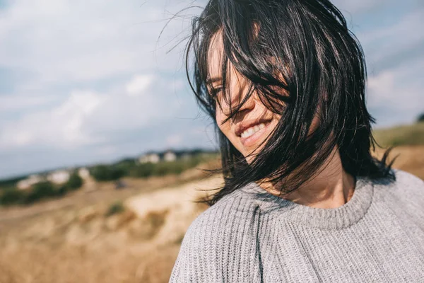 Horizontale bijgesneden portret van mooie lachende vrouw dragen trui wezen speels met haar winderige en zorgeloze poseren op zonlicht hemel en natuur achtergrond. Reizen, mensen en levensstijl concept. — Stockfoto