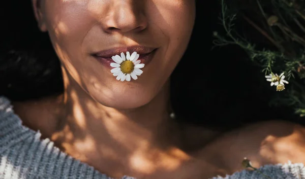 Recortado de cerca plano horizontal de chica joven morena con flores de margarita en la boca al aire libre disfrutando de la naturaleza. Retrato de una atractiva mujer caucásica siéntase libre con espacio de copia. Estado de ánimo idea cubierta — Foto de Stock