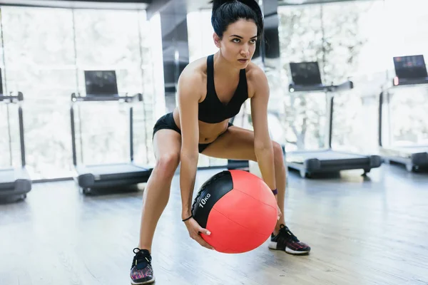 Mujer atlética muscular haciendo sentadillas de entrenamiento en el gimnasio. Fuerte sentadilla femenina en la alfombra de fitness con balón de medicina de peso en el club de salud. Deporte, personas y estilo de vida . — Foto de Stock
