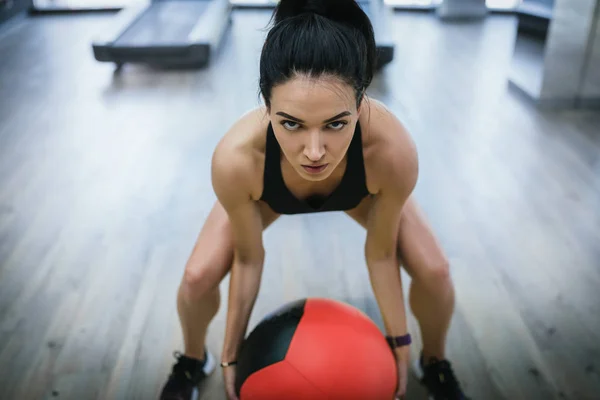 Detailní záběr fit žena dělá intenzivní základní cvičení v tělocvičně. Mladý svalnatý žena dělá základní cvičení a dřepu na fitness mat v health club s lékařství míč. — Stock fotografie
