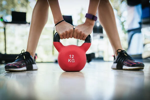 Cropped shot of young fitness woman doing swing exercise with a kettle bell as a part of a fitness workout in the gym or fitness club. Beautiful legs with kettle bell.