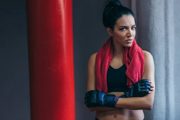 Portrait of pretty attractive brunette sportswoman with red towel on neck after workout with punch bag, cross the hands wearing kickboxing gloves in the gym. Sport, fitness, lifestyle, people concept. — Stock Photo, Image
