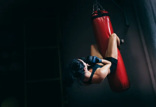 Rear view of young beautiful sportswoman working at her abdominal muscules on a red punching bag on dark background. Sport, fitness, lifestyle, people and motivation concept. — Stock Photo, Image