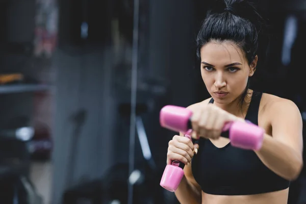 Ritratto orizzontale di giovane donna forte che fa esercizio con manubri. Fitness femminile europea che fa un intenso allenamento nel club di ginnastica. Sport, persone, motivazione e sano concetto di stile di vita . — Foto Stock