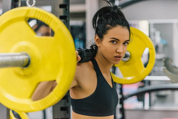 Mooie jonge vrouw training in de sportschool, gele barbell te duwen op de schouders. Vrouwelijke harde training voor cross fit. Mensen, sport, fitness, gezonde levensstijl en motivatie concept. — Stockfoto