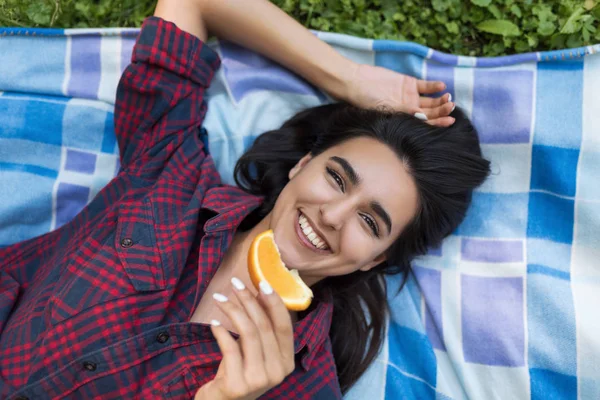 Øverste utsikt over vakker, pen brunette smilende kvinne med saftig oransje i sommerens grønne park. Unge, sunne kvinnesmiler som nyter og holder appelsinfrukt for vegetarisk livsstil . – stockfoto