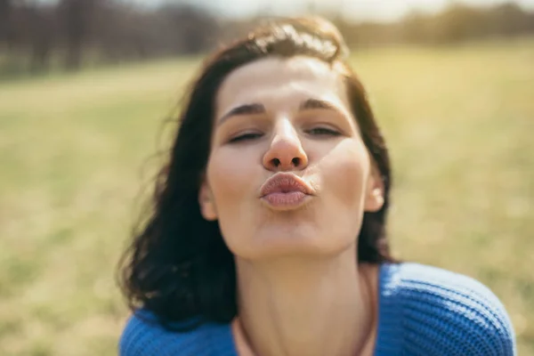 Close up portrait of attractive happy young woman being playful and carefree with beautiful kiss on sunny day. Lifestyle concept. Happy female portrait on summer or spring day outside in park. Fun day