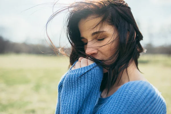 Close up portrait of attractive brunette caucasian young woman traveler with windy hair, dreaming outside, on spring or on summer, in park. Dreamy female with closed eyes in blue pullover. Lifestyle. — Stock Photo, Image