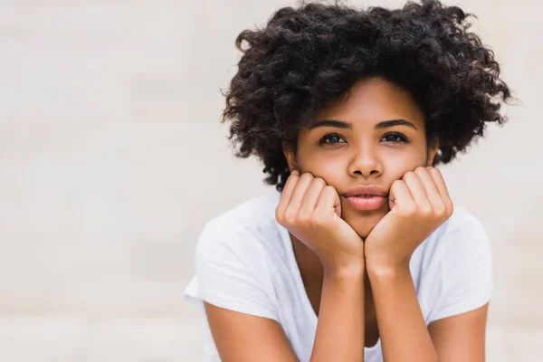 Portrait de belle afro-américaine jeune femme à la peau foncée avec une coiffure shaggy assis aigthe light wall background outdoor. Style de vie et concept de personnes . — Photo