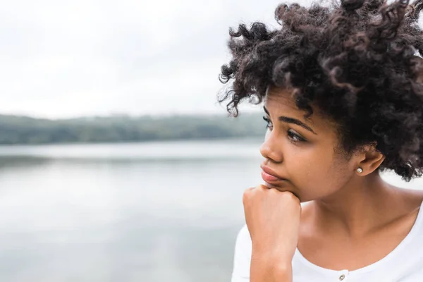 Primer plano de la joven mujer negra con mirada pensativa, contra el fondo de la naturaleza con espacio de copia para su texto o contenido publicitario. Retrato de una mujer de piel oscura que lleva una pose casual al aire libre —  Fotos de Stock