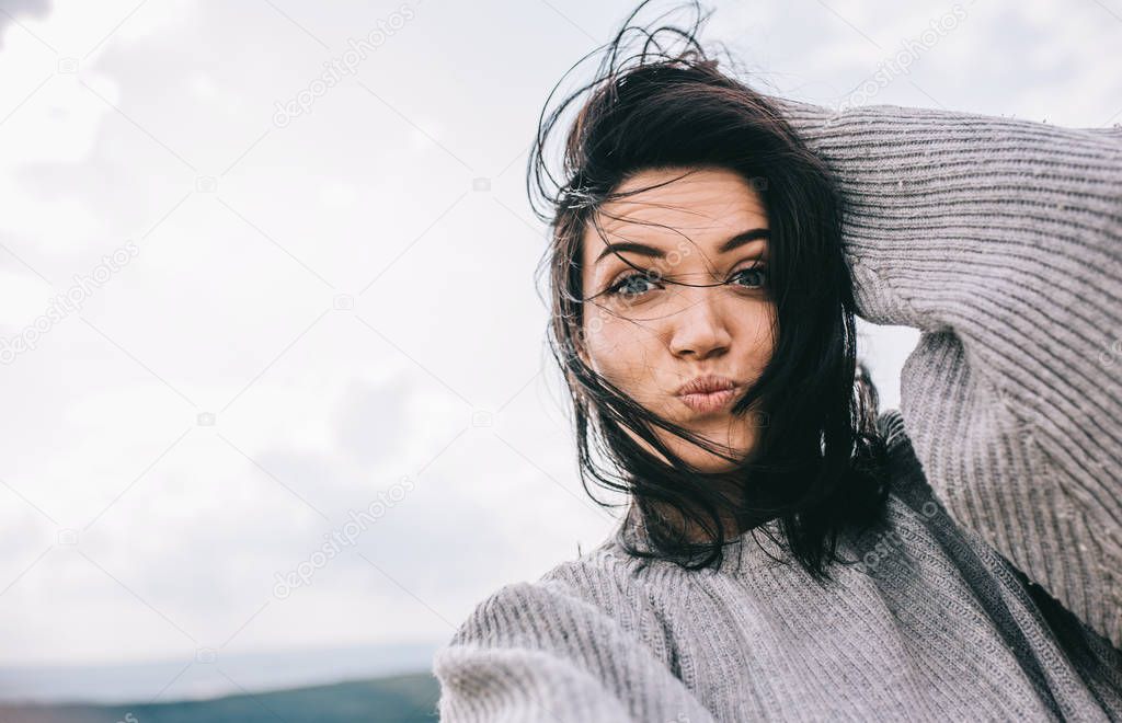 Bottom view of happy and funny brunette woman taking self portrait and blowing kiss on sunlight background. Cute female take selfie from her device. People, travel and lifestyle concept. Cover mood.