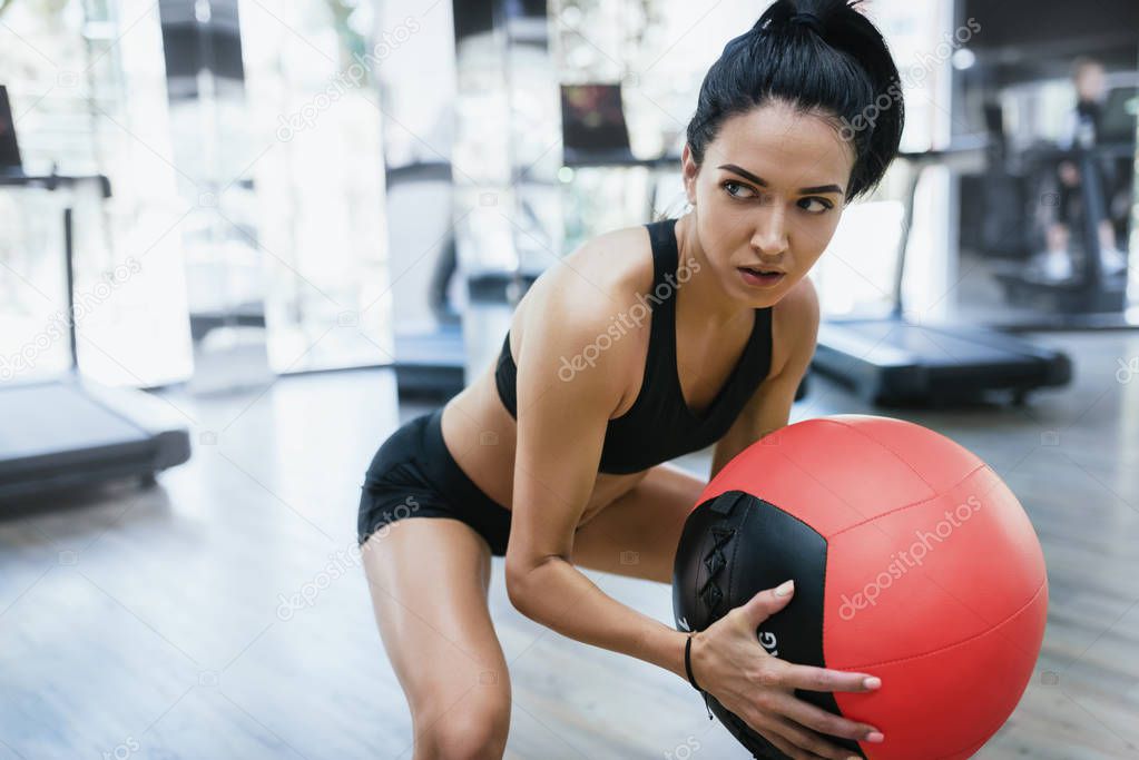 Portrait of muscular athletic woman doing squats workout in gym. Strong female squatting  on fitness mat with weight medicine ball in health club. Sport, people and lifestyle concept.