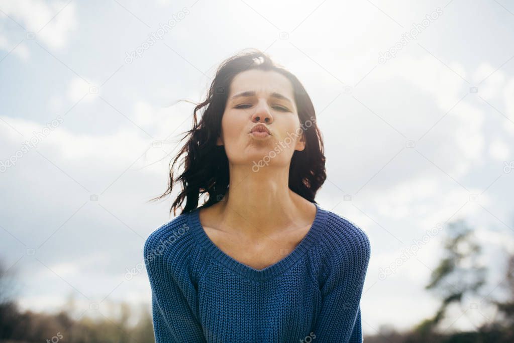 Bottom view portrait of beautiful young brunette woman kiss with the wind blowing hair on nature background. Attractive cheerful girl enjoy sun in park. Lifestyle concept. Cover idea concept.