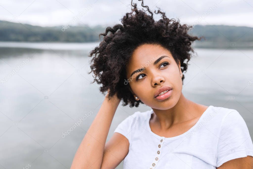 Beautiful young black woman with pensive, reflective look, against nature background with copy space for your text or advertising content. POrtrait of dark-skinned female wearing casual posing outdoor