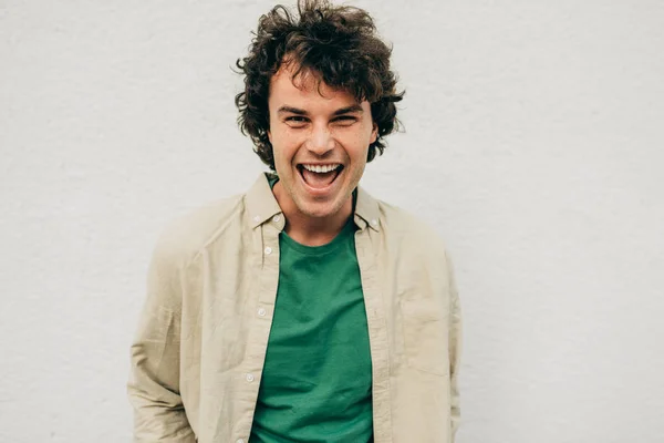 Horizontal portrait of handsome young man posing for advertisement, smiling and looking at the camera, standing at building concrete wall outdoors. Portrait of happy smart student male with curly hair — Stock Photo, Image