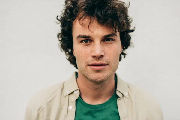 Retrato de close-up de belo jovem posando para propaganda, olhando para a câmera, em pé na construção de parede de concreto ao ar livre. Retrato de estudante inteligente feliz macho com cabelo encaracolado — Fotografia de Stock