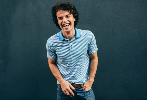 Imagem de jovem alegre posando para propaganda, sorrindo e olhando para a câmera, de pé na construção de parede de concreto ao ar livre. Retrato de estudante feliz do sexo masculino posando fora. Pessoas e emoção — Fotografia de Stock