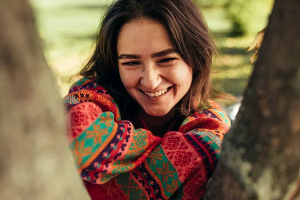 Portrait of happy brunette young woman with freckles smiling and enjoying the weather, wearing sweater on nature background. Stylish female smiling posing in the park on sunny day. — Stock Photo, Image