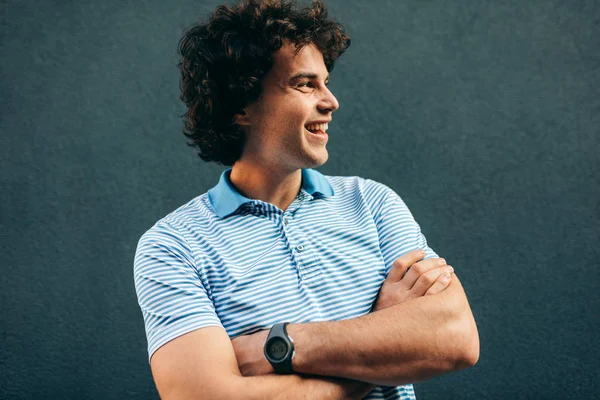 Retrato de jovem alegre posando para propaganda, sorrindo e olhando para um lado, em pé na parede de concreto ao ar livre. Retrato de estudante inteligente feliz masculino tem expressão positiva . — Fotografia de Stock