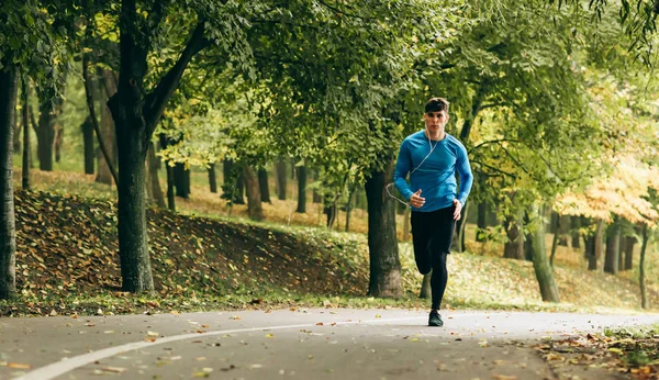 Горизонтальное полное изображение тела молодого бегуна, бегущего на свежем воздухе в лесу. Мужчина занимается в парке, в синей и черной одежде. Люди и спорт — стоковое фото