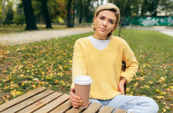 Mulher bonita bebendo café no terraço café no parque. Retrato de jovem na rua da cidade bebendo cappuccino quente, olhando para a câmera. Mulher bonita com xícara de café. Café em movimento . — Fotografia de Stock
