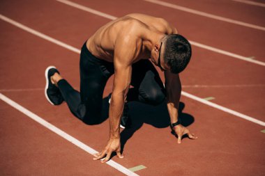 Stadyumdaki hipodromda koşmaya hazırlanan üstsüz bir sporcunun görüntüsü. Formda erkek koşucu yarışma için antrenman sırasında koşuyor. İnsanlar, spor ve sağlıklı yaşam tarzı