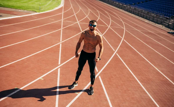 Jonge atleet die poseert op een racebaan in het stadion. Professionele shirtloze sportman bereidt zich voor op trainingssessie. Mensen, sport en een gezonde levensstijl — Stockfoto