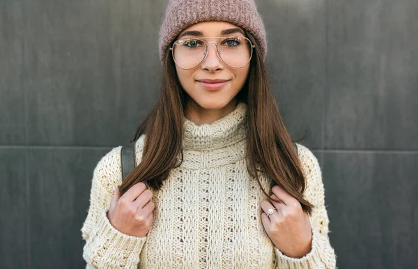 Close-up retrato de bela jovem sorridente olhando diretamente para a câmera, andando na rua da cidade, vestindo suéter de malha, chapéu rosa e óculos transparentes . — Fotografia de Stock