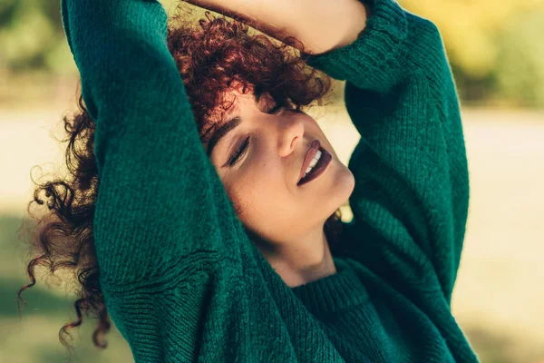 Close-up retrato de bela jovem mulher sorrindo posando contra o fundo da natureza com cabelo encaracolado ventoso, tem expressão positiva, vestindo em suéter verde. Pessoas, viagens e estilo de vida . — Fotografia de Stock