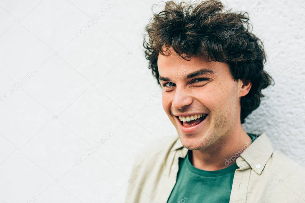 Close-up portrait of happy handsome young man smiling broadly posing for advertisement, smiling and looking at the camera. Portrait of attractive male with curly hair has joyful expression.