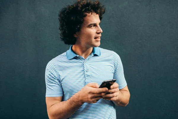 Joven hombre inteligente navegando en la web en el teléfono móvil. Hombre guapo con el pelo rizado descansando afuera haciendo una llamada en su teléfono inteligente en la calle de la ciudad. Estilo de vida, gente — Foto de Stock