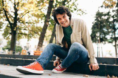 Yakışıklı genç adam gülümsüyor, kameraya bakıyor ve merdivenlerde oturuyor. Mutlu zeki öğrenci erkek dışarıda dinleniyor. İnsanlar ve duygu kavramı