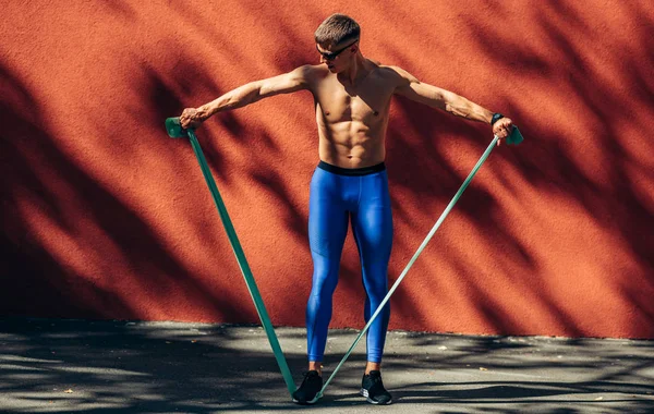 Atleta hombre estiramiento antes de los ejercicios al aire libre contra la pared de hormigón rojo. Ajuste los estiramientos masculinos después del entrenamiento afuera. Concepto deporte y personas . — Foto de Stock