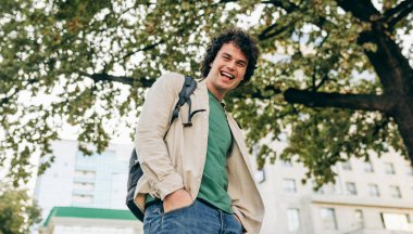 Smiling man with curly hair, posing for social advertisement, posing on the city street. Excited cheerful student male has joyful expression.