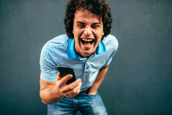 Изображение счастливого молодого человека с вьющимися волосами, смеющегося и разговаривающего по мобильному телефону со своей девушкой, имеет радостное выражение. Веселый мужчина широко улыбается во время звонка на свой смартфон на улице . — стоковое фото