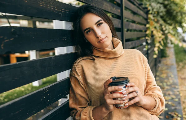 Mulher bonita bebendo café em movimento na rua da cidade. Uma mulher bonita na rua da cidade a beber cappuccino quente. Menina morena bonita com xícara de café . — Fotografia de Stock