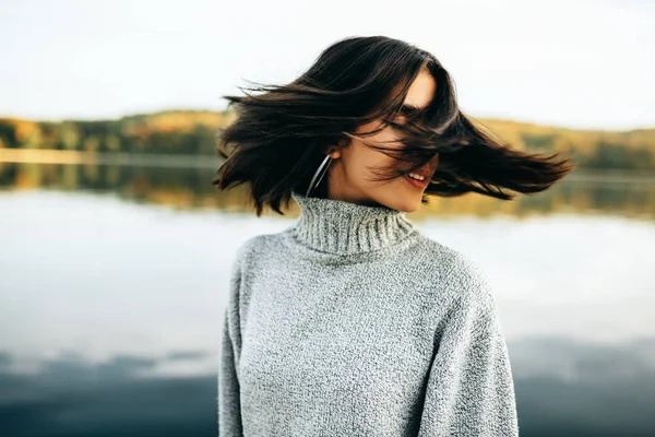 Imagem de jovem morena feliz com os olhos fechados, vestindo camisola cinza, posando no fundo da natureza. Menina bonita posando contra o lago no parque . — Fotografia de Stock