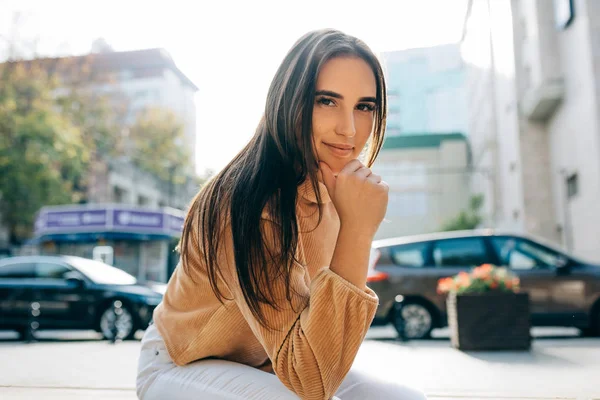 Young brunette woman wearing casual outfit, smiling and looking directly to the camera, taking rest outside. Pretty female relaxing in the city street. — Stock Photo, Image