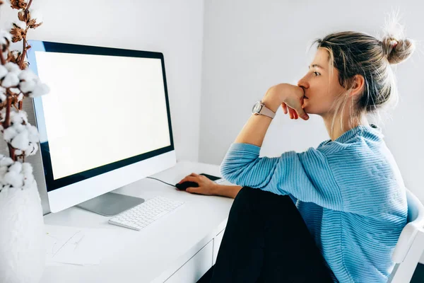 Imagem de vista lateral de empresária freelancer usando um computador desktop em um escritório. Jovem loira se senta dentro de casa trabalhando no computador com uma tela em branco para sua mensagem de texto ou conteúdo . — Fotografia de Stock