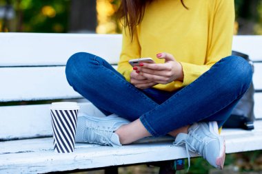 Satışlar sırasında akıllı telefonu elinde tutan bir kızın kırpılmış görüntüsü. Sosyal medyada arkadaşlarıyla konuşurken cep telefonu kullanan genç bir kadın dışarıda kahve içiyor.