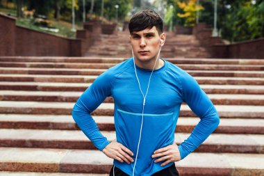 Sabahları dışarıda poz veren yakışıklı genç bir atlet. Koşu sırasında sisli doğa arka planında. Kaslı erkek parkta egzersiz yapıyor ve kulaklıkla müzik dinliyor. Millet, spor konsepti