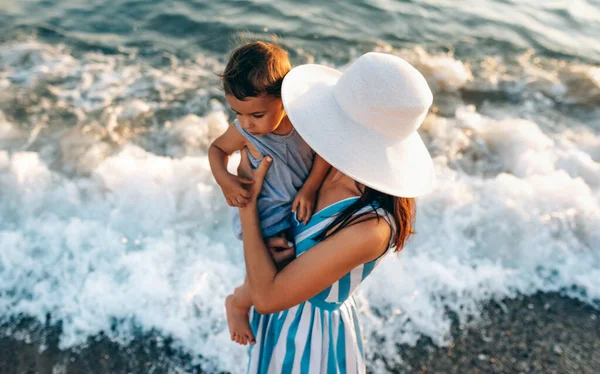 어머니가 줄무늬 드레스를 모자를 바닷가에서 과놀고 수평으로 위에서 보인다 곳에서 — 스톡 사진